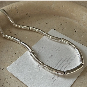 Detail of minimalist S925 sterling silver tube link necklace on a ceramic plate