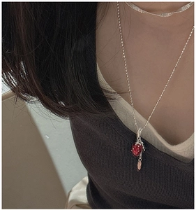 Close-up of a silver strawberry pendant necklace with red crystal on a model collarbone