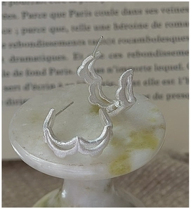 Macro shot of S925 silver wave earrings with brushed texture on a marble stand
