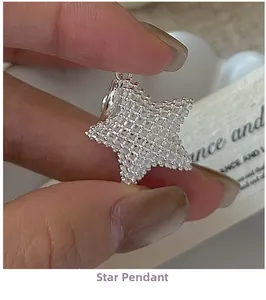 Detailed macro view of a 3D grid textured silver star pendant held by fingers