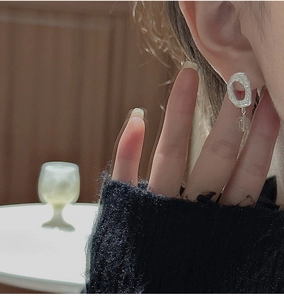 Detail of silver matte earrings with irregular lava texture and a clear crystal drop