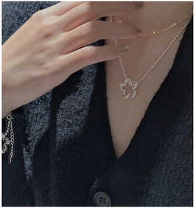 Close-up of layered S925 silver flower pendant necklace on a neck with black knit sweater