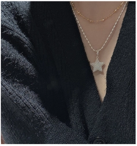 Close-up of layered silver star pendant and gold beaded chain on black knitwear