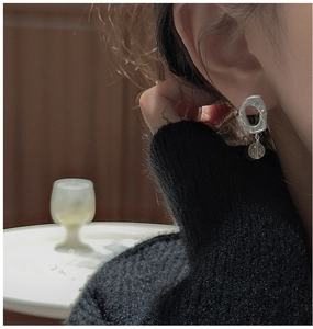 Detail of matte silver drop earring with hammered oval hoop and clear bead on model