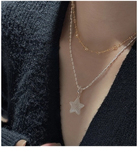 Detail of layered S925 silver star pendant necklace and gold bead chain on a model