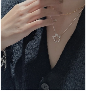 Detail of silver floral hollow pendant and beaded chain on a model wearing black knitwear