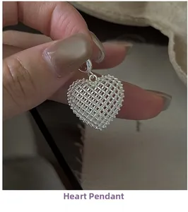 Macro shot of a 3D hollow mesh heart pendant in polished silver held by fingers