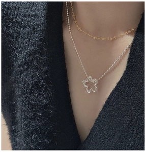Detail of S925 silver flower pendant layered with golden beaded necklace on black apparel