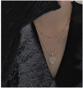 Detail of a layered silver necklace featuring a filigree hollow heart pendant on a twist chain
