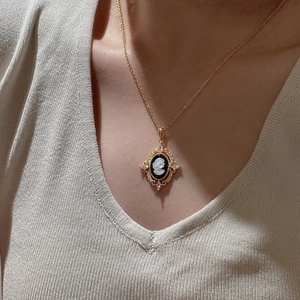 Vintage gold cameo pendant necklace with zircon accents on beige knitwear background