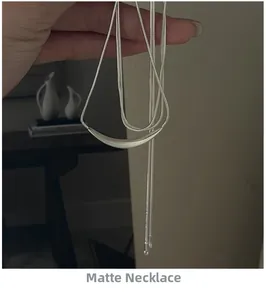 Gros plan d'un collier mat argenté avec pendentif tube courbé et chaîne serpent fine