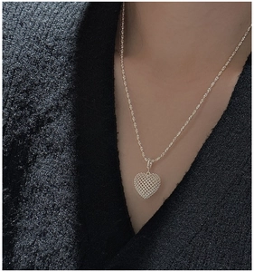 Detail of 3D hollow mesh heart pendant on a fine silver chain against black tweed fabric