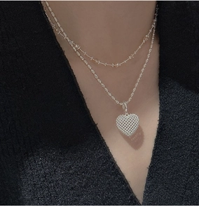Detail of 3D hollow heart grid pendant on double layered silver necklace worn by model