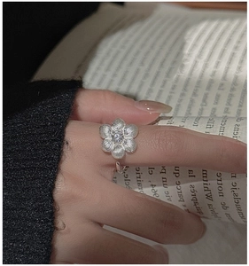 Detail of a matte silver floral ring with a central zircon stone and brushed texture