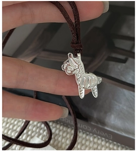 Detail of silver zebra pendant on brown suede cord held against a white knit background