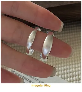 Macro detail of two minimalist irregular matte S925 silver wave rings on a finger
