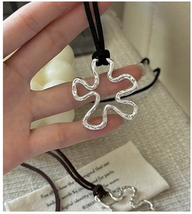 Detailed view of silver irregular wavy flower pendant on a black cord necklace