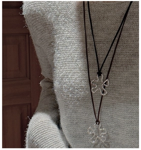 Detail of the irregular silver flower pendant on a black cord worn over a knit sweater