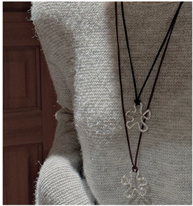Detail of silver wavy flower pendants on dark cords layered over a beige knit sweater