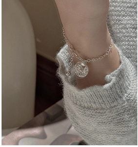 Detail of S925 silver chain bracelet with round textured pendant on a knit sleeve