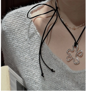 Detail of silver irregular flower pendant on black ribbon styled with grey sweater