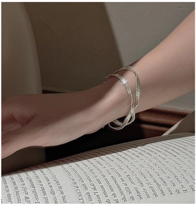 Detail of minimalist silver woven spiral bracelet worn by a model in a cozy setting