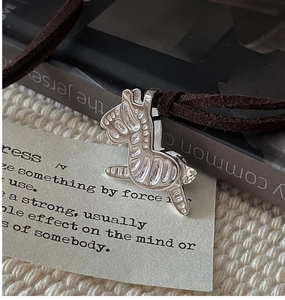 Detailed view of silver horse pendant with brown suede cord on cream knit background