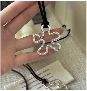 Detail of silver wavy flower pendant with handmade hammered texture on black cord necklace