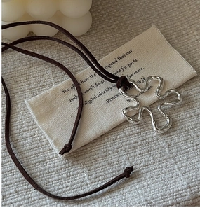 Detail view of silver wavy flower pendant with brown suede cord on linen bag texture