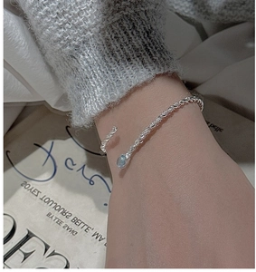 Detail of twisted silver bangle with a light blue gemstone on a neutral background