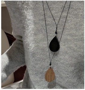 Detail of drop-shaped wood grain and matte black pendant necklace on a grey sweater