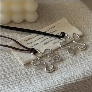 Macro shot of silver flower pendant with black suede cord on cream fabric background