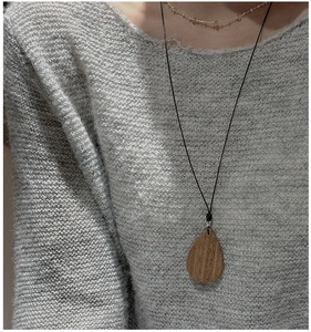 Close-up of a teardrop wood pendant necklace with silver clasp on a grey knit sweater