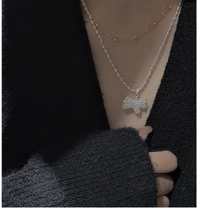 Close-up of layered silver and gold chains with hollow terrier puppy pendant on model