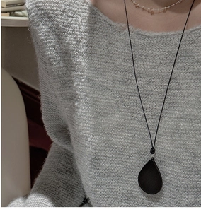 Close-up of minimalist black teardrop pendant on long cord with grey sweater texture