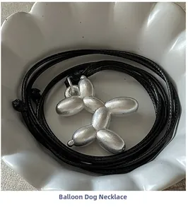 Gros plan du pendentif chien ballon argenté mat sur cordon noir et assiette blanche