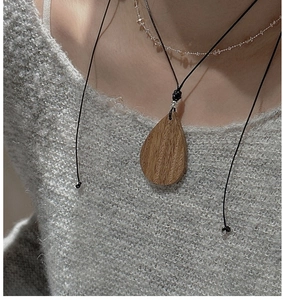 Macro detail of teardrop wooden pendant necklace with natural grain on grey sweater