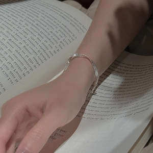 S925 sterling silver woven bracelet with pleated texture on wrist over a book