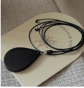 Detail view of a black teardrop pendant necklace with silver beads on floral card