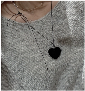 Detail of a black heart pendant necklace layered with beads over a grey knit sweater