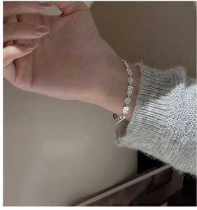 Detail of silver geometric matte disc bracelet worn on wrist with grey knitwear
