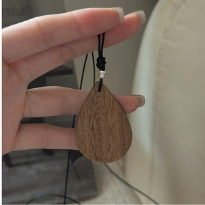 Macro shot of waterdrop shaped dark brown wood pendant with natural grain on black cord