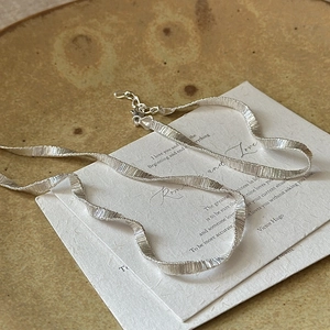 Elegant S925 sterling silver wavy flat chain necklace with textured finish on ceramic tray