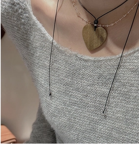 Detail of S925 silver heart pendant with wood grain texture on grey knitted sweater