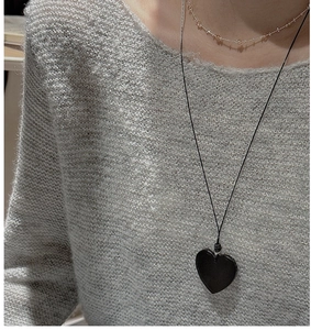 Close-up of a minimalist black heart pendant necklace on a grey knitted sweater texture