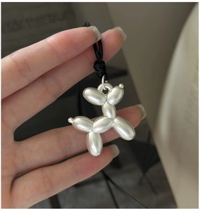 Vue macro d'un pendentif chien ballon argent mat tenu à la main avec cordon noir