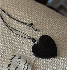 Close-up of minimalist black heart pendant on rope necklace over beige linen background