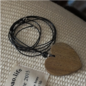 Detail of a dark wood heart pendant with natural grain on a woven textile background