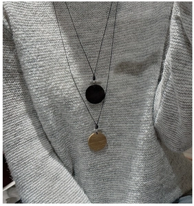 Détails de pendentifs ronds en grain de bois sur cordons noirs sur un pull en tricot gris