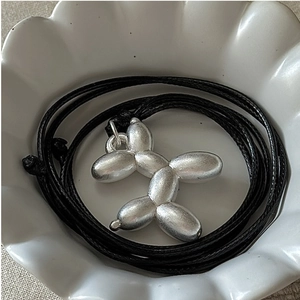 Détail d'un pendentif chien ballon argenté sur cordon noir dans une coupelle blanche